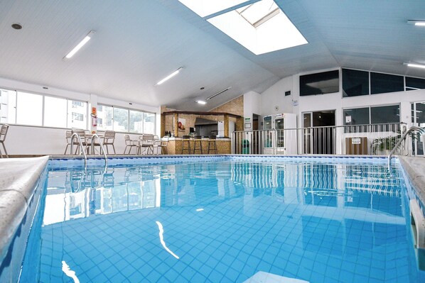En inomhuspool med kaklade väggar, en bardisk och utsikt över staden genom stora fönster.