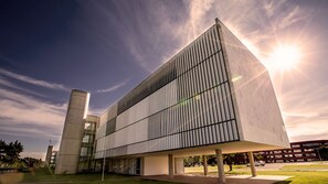 Un edificio moderno con techo plano, ventanas amplias y una estructura cilíndrica destacada a la izquierda.