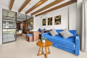A modern living room with a blue sofa, a wooden coffee table, and a glass partition. - Vantara by Kozystay - Nusa Dua (Badung)