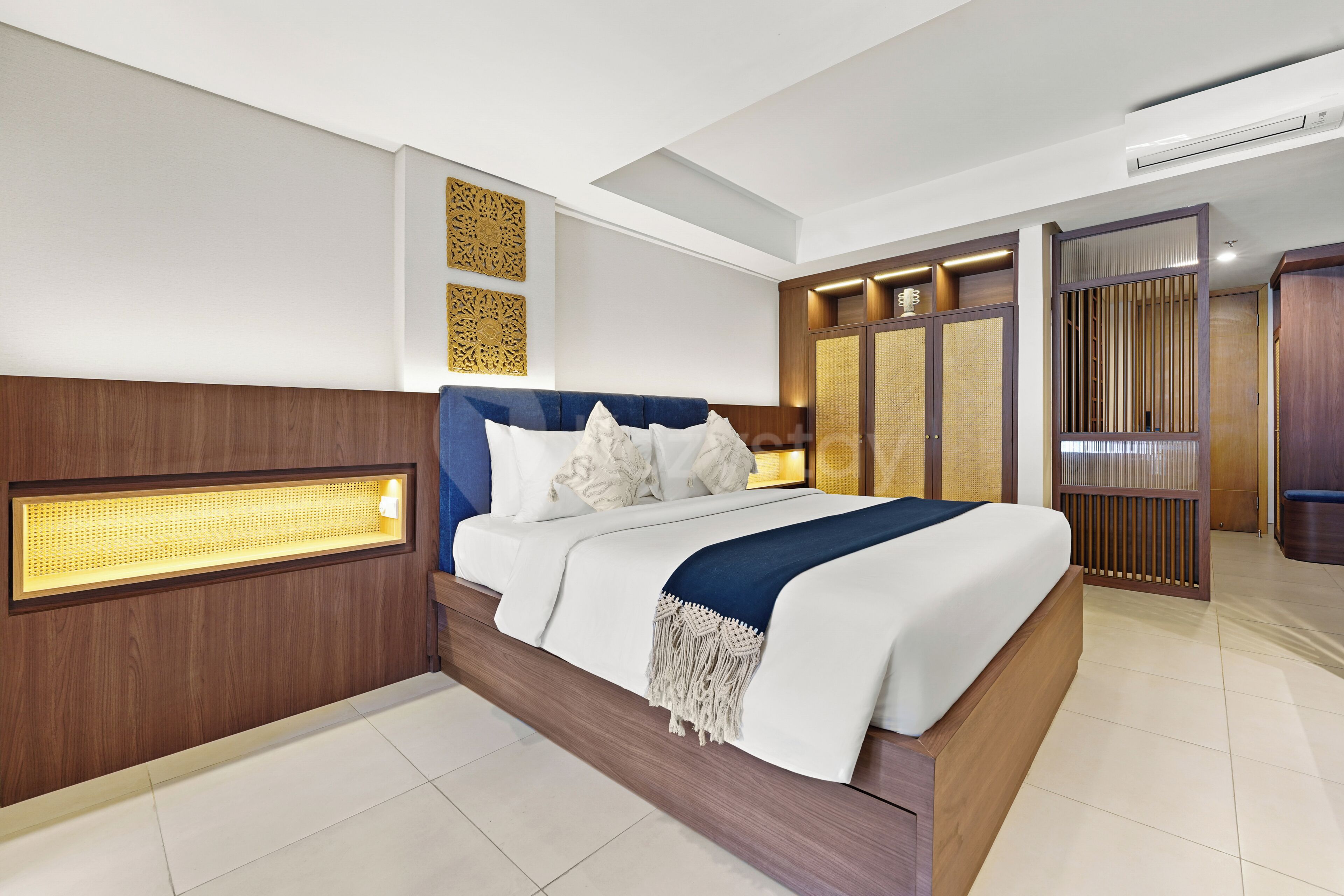 A modern hotel room with a large bed, wooden headboard, decorative wall panels, and a built-in wardrobe with a sliding door.