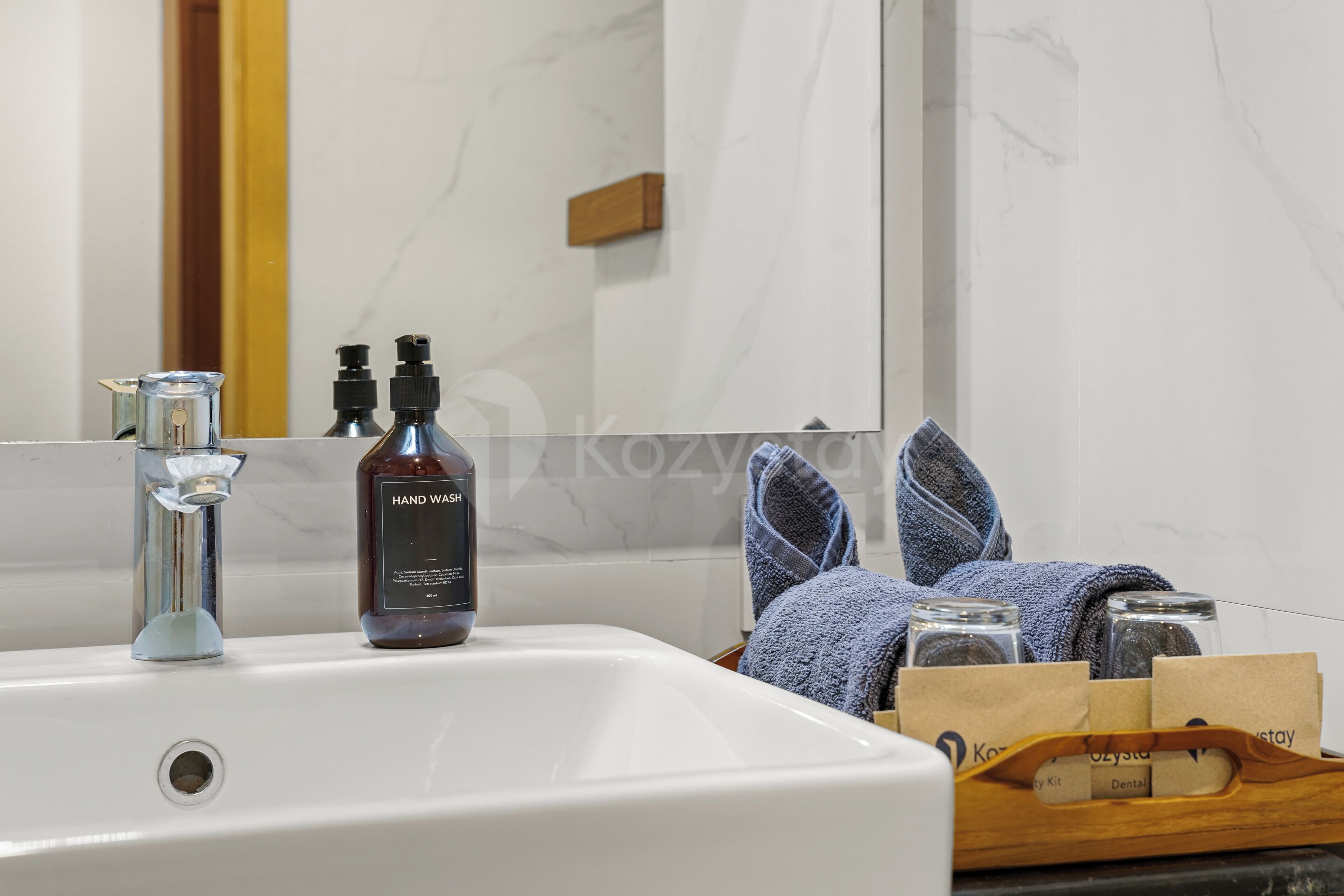 A bathroom with a white sink, two hand wash bottles, a towel, and a wooden tray with toiletries.