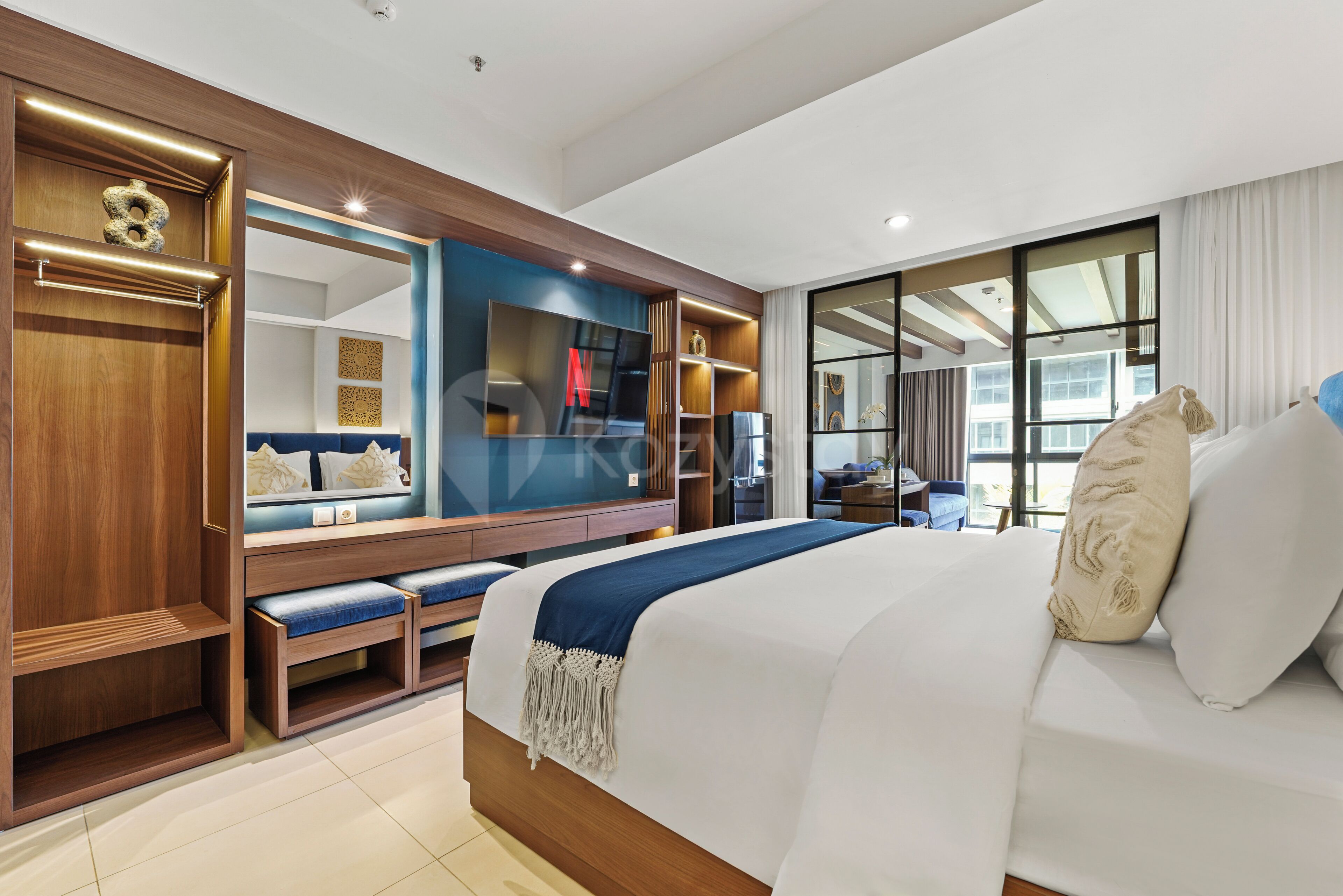 Une chambre d’hôtel moderne dotée d’un grand lit, d’un coin salon avec un banc, d’une télévision et d’une grande fenêtre.
