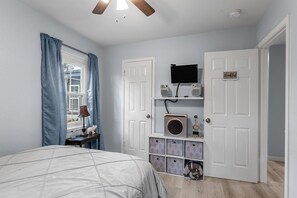 A bedroom with a bed, a desk, a lamp, a television, and storage boxes.