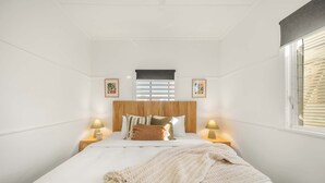 Quarto com uma cama, duas luminárias de cabeceira, uma janela com persianas e dois quadros na parede.