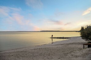 A beach with calm waters, a person fishing, and a distant shoreline. - Aloha Sands - Golden Beach Escape, Dog-Friendly (Caloundra Region)