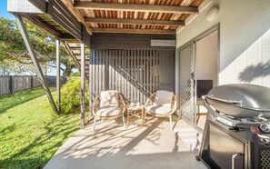 Eine Terrasse im Freien mit Grill, Korbstühlen und einer Pergola.