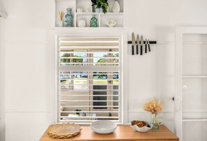 A kitchen with a window, a wooden table with a bowl and a plate, and a knife rack. - Aloha Sands - Golden Beach Escape, Dog-Friendly (Caloundra Region)