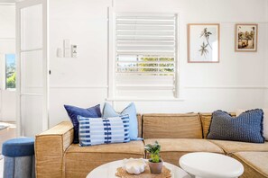 A living room with a beige sofa, blue and white patterned pillows, a small potted plant, and a white round table with a white object on it. - Aloha Sands - Golden Beach Escape, Dog-Friendly (Caloundra Region)