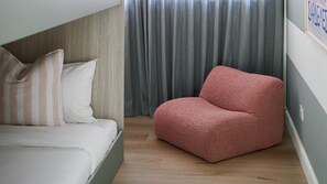 Une chambre à coucher avec un lit, un fauteuil rouge recouvert de tissu, un plancher en bois et un rideau gris.