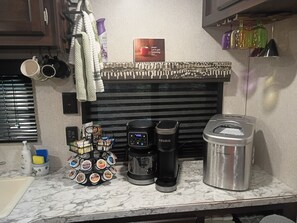 Eine Küchenzeile mit Kaffeemaschine, Wasserkocher, Tassenhalterung und Kapselbehälter.