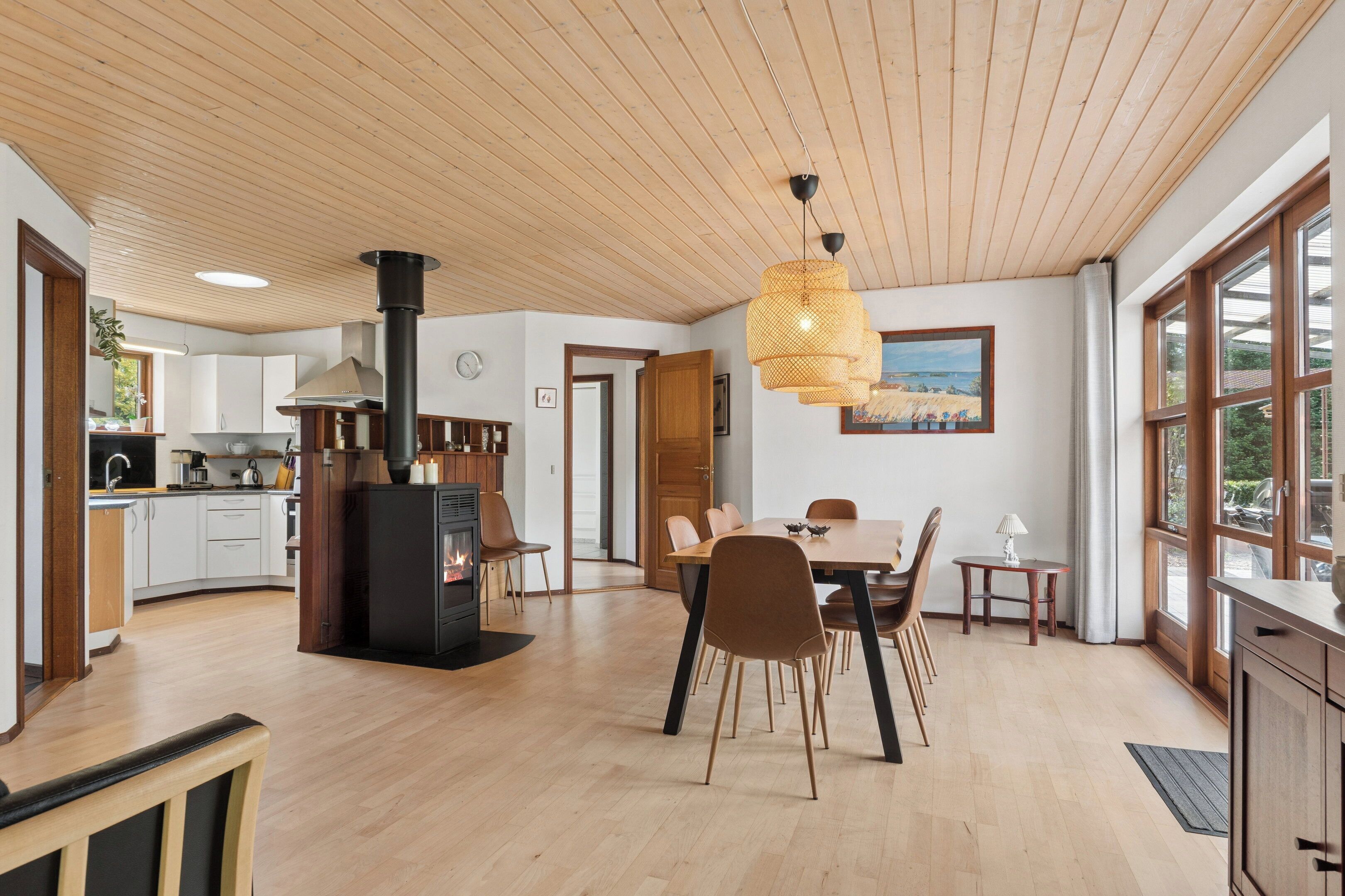 Een moderne keuken met een houtkachel, een eethoek met stoelen en grote ramen.