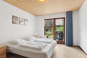 Quarto com duas camas, janela com vista para o verde e teto de madeira.