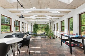 Amplo espaço interno com mesa de pebolim, assentos e grandes janelas.