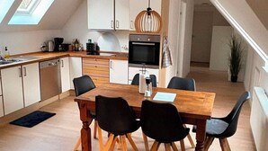 A modern kitchen with a dining area, featuring a wooden table and chairs, a built-in oven, and a skylight. - Scenic home in Virklund (Virklund)