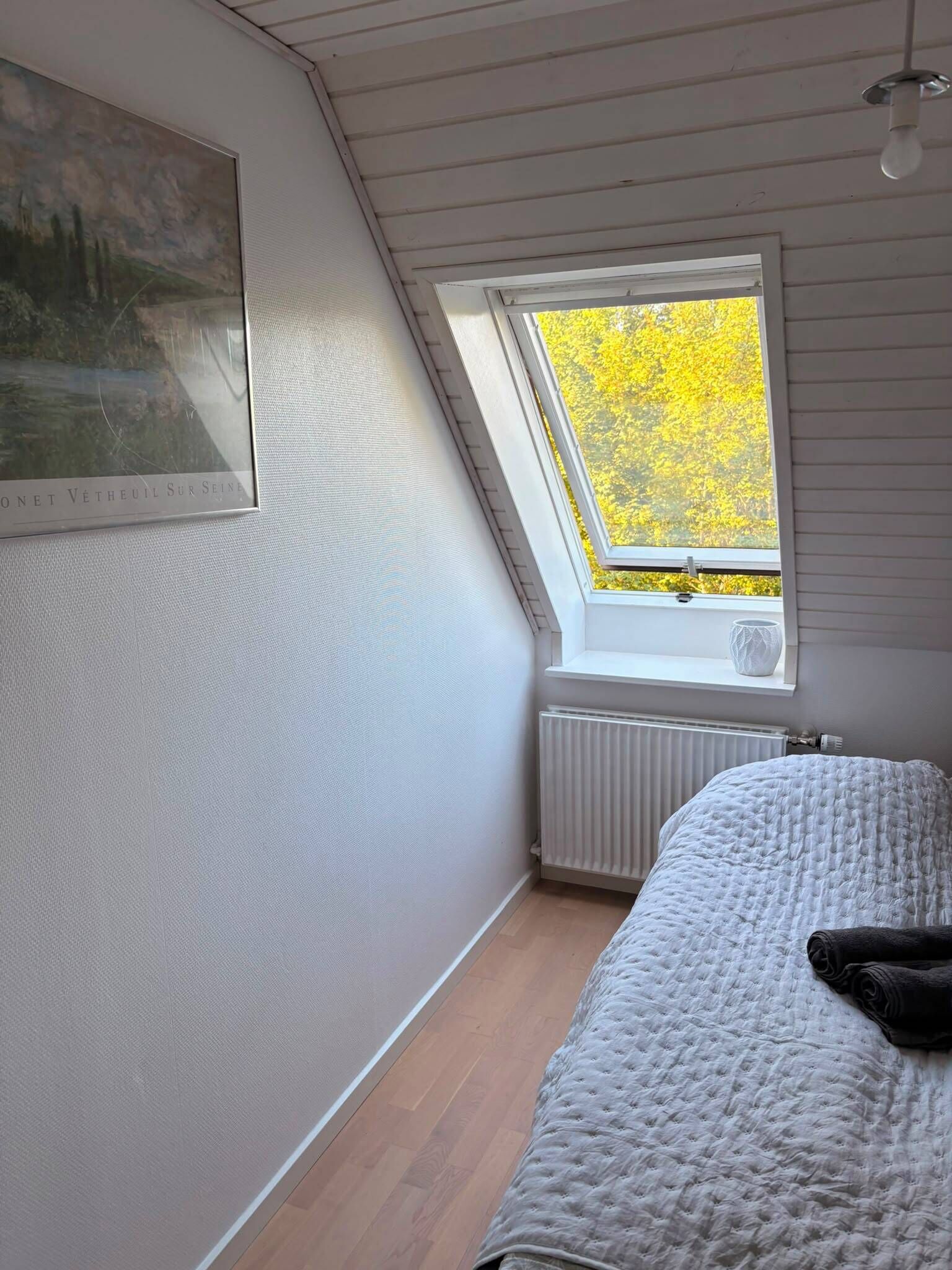 A bedroom with a sloped ceiling, a skylight, a radiator, and a bed with a rolled-up blanket.