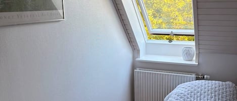 Et soveværelse med skråvæg, ovenlys, radiator og en seng med et sammenrullet tæppe.