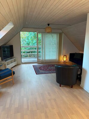 Ein geräumiges Wohnzimmer mit Fernseher, einer Couch, einem Sessel und einer Stehlampe.