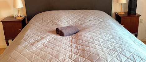 A bed with a quilted headboard, a rolled towel, and two bedside tables with lamps.