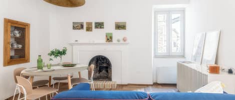 A room with a fireplace, a dining table with chairs, a sofa, and artwork on the walls.