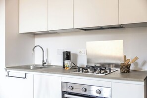 A kitchen with a stainless steel sink, a coffee maker, a gas stove, and wooden utensils in a woven basket. - Italian Experience - Suite Sinfonia Oro (Bevagna)