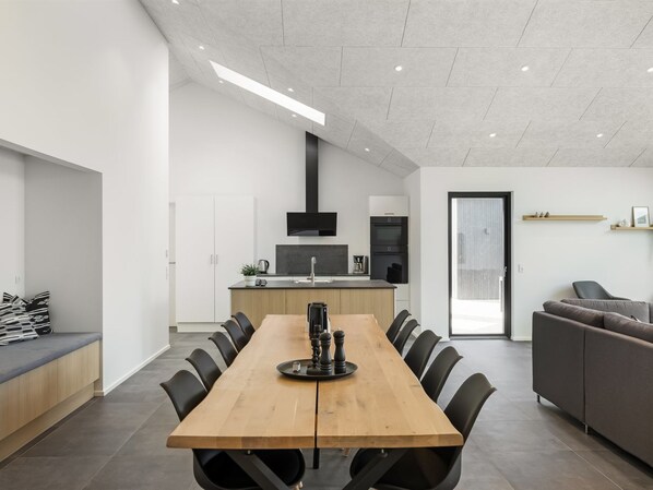 A modern kitchen with a central island, a dining area with a long table, and a seating area with a sofa.