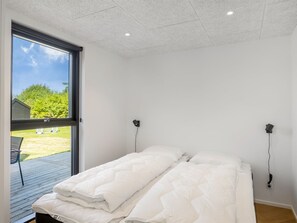 A bedroom with a bed, two wall-mounted lamps, a window, and a view of a green landscape.
