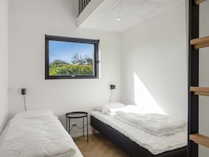 Een moderne slaapkamer met twee bedden, een raam met uitzicht op groen en een klein, rond tafeltje.