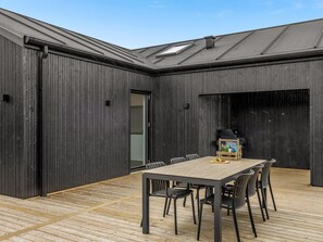 A modern outdoor dining area with a wooden deck, a table with chairs, and a grill.