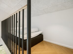 Een moderne slaapkamer met een bed, een bankje en een trap met zwarte leuningen.