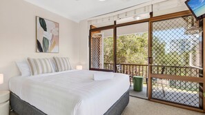Une chambre à coucher avec un lit, un tableau, une porte-fenêtre coulissante donnant sur un espace extérieur et une vue sur la verdure.
