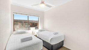 Ein Schlafzimmer mit zwei Betten, einem Deckenventilator und einem Fenster mit Blick auf Gebäude.