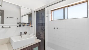 Ein modernes Badezimmer mit einem weißen Waschbecken, einem Spiegel und einer Duschkabine.