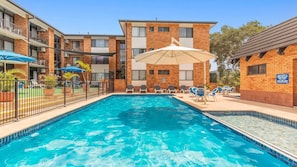Ein Swimmingpool mit Liegestühlen und Sonnenschirmen, umgeben von Gebäuden mit Balkonen.