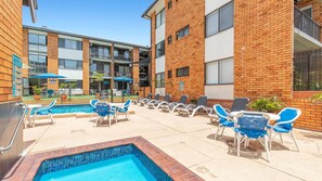 A pool area with lounge chairs and a hot tub, surrounded by brick buildings with balconies. - Sandcastles 213 - across the street from Park Beach in Coffs Harbour (Coffs Harbour)