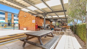 Un'area patio esterna con tavoli da picnic e una griglia per barbecue, accanto a un edificio in mattoni con un cartello di avvertimento.