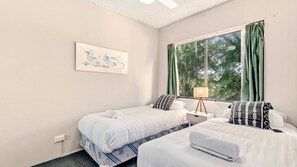 A hotel room with two beds, a bedside table, a lamp, a window with curtains, and a framed picture on the wall. - Sandcastles 213 - across the street from Park Beach in Coffs Harbour (Coffs Harbour)