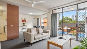 Un salon moderne avec un canapé, une table basse et une vue sur une piscine, visible à travers de grandes fenêtres.