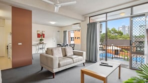 Ein modernes Wohnzimmer mit einer Couch, einem Couchtisch und Blick auf einen Swimmingpool durch große Fenster.