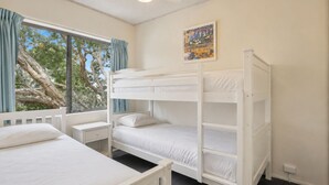 Une chambre avec des lits superposés, une fenêtre avec des rideaux, une table de chevet et un tableau accroché au mur.