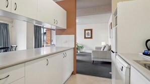 Une cuisine moderne avec des meubles blancs et un plan de travail gris, qui s’ouvre sur un espace de vie comprenant un canapé et une table basse.