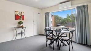Una habitación con una mesa de comedor, sillas, una mesita auxiliar con una planta y un ventanal con cortinas.