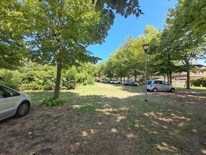 A parking area with cars and trees, a lamp post, and a building in the background. - A cozy place for a beach vacation for nice people (and their pets) (Lido degli Scacchi)