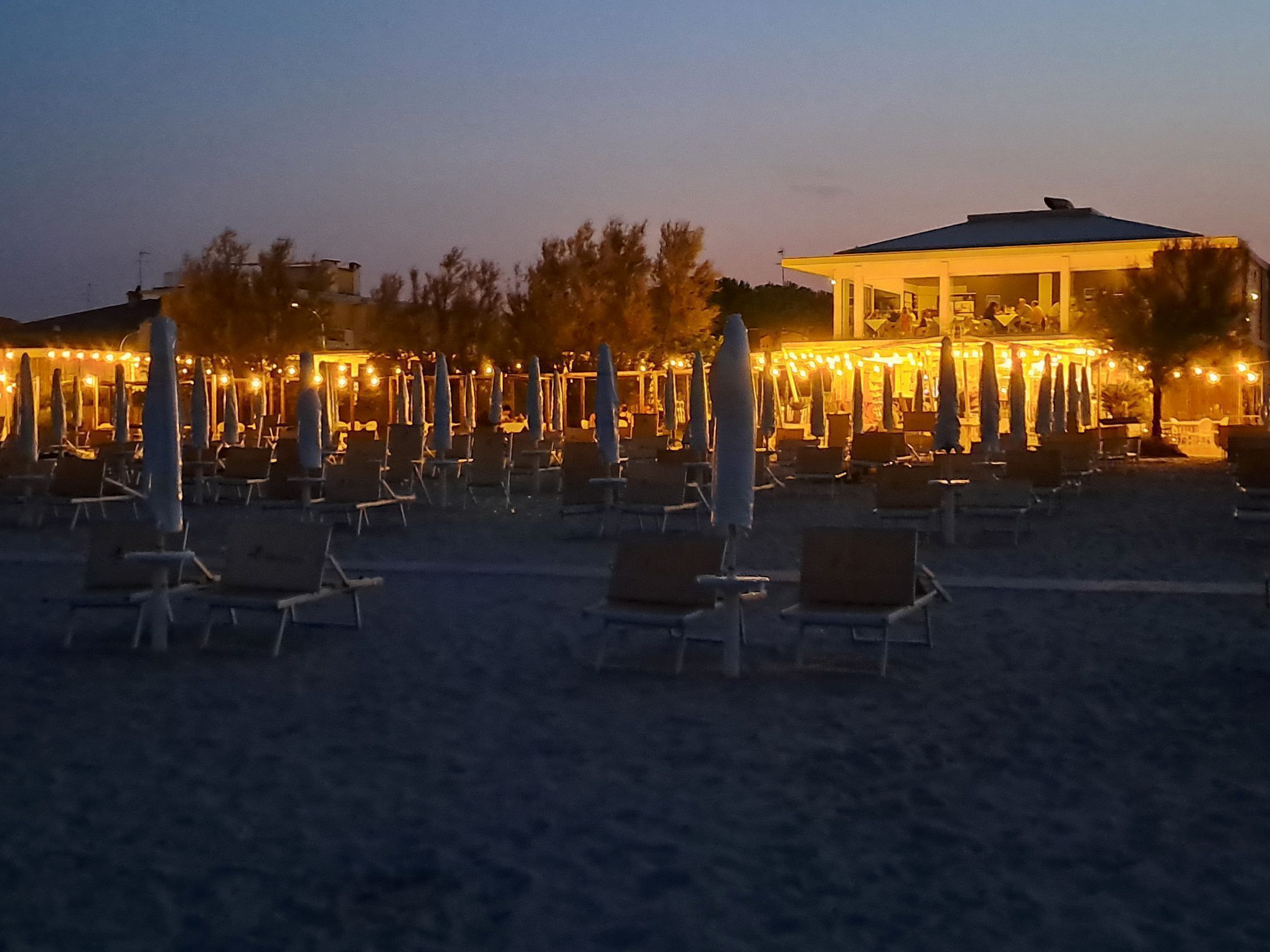 A beachside resort with rows of sun loungers and umbrellas, a building with a covered area, and a clear sky.