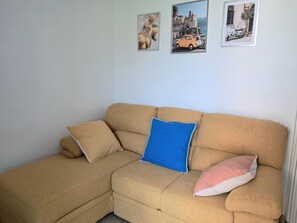 A beige sectional sofa with three pillows, a white wall, and three framed pictures.