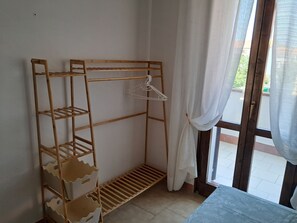 A wooden wardrobe with multiple shelves and a hanging rod, positioned next to a window with a curtain.