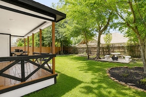 A backyard with a wooden deck, a barbecue grill, and a stone fire pit. - Cozy Modern Tomball Home, Family-Friendly & Spacious Backyard (Tomball)