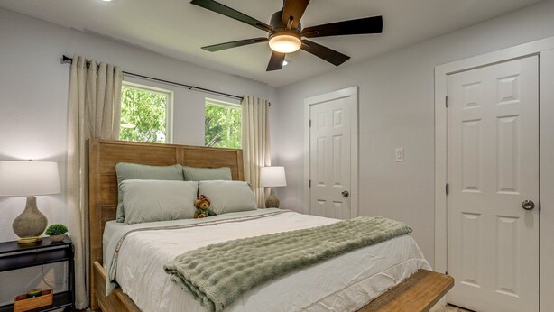 Quarto com cama, abajures, ventoinha no teto e um banco.