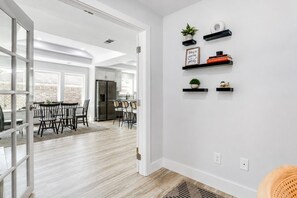 A modern kitchen with a dining area, featuring a refrigerator, chairs, and a view through an open door.