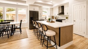 Uma cozinha moderna com uma ilha central, banquetas de bar e uma área de refeições com mesa e cadeiras.