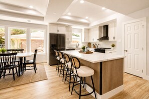 A modern kitchen with a central island, bar stools, and a dining area with a table and chairs. - Cozy Modern Tomball Home, Family-Friendly & Spacious Backyard (Tomball)